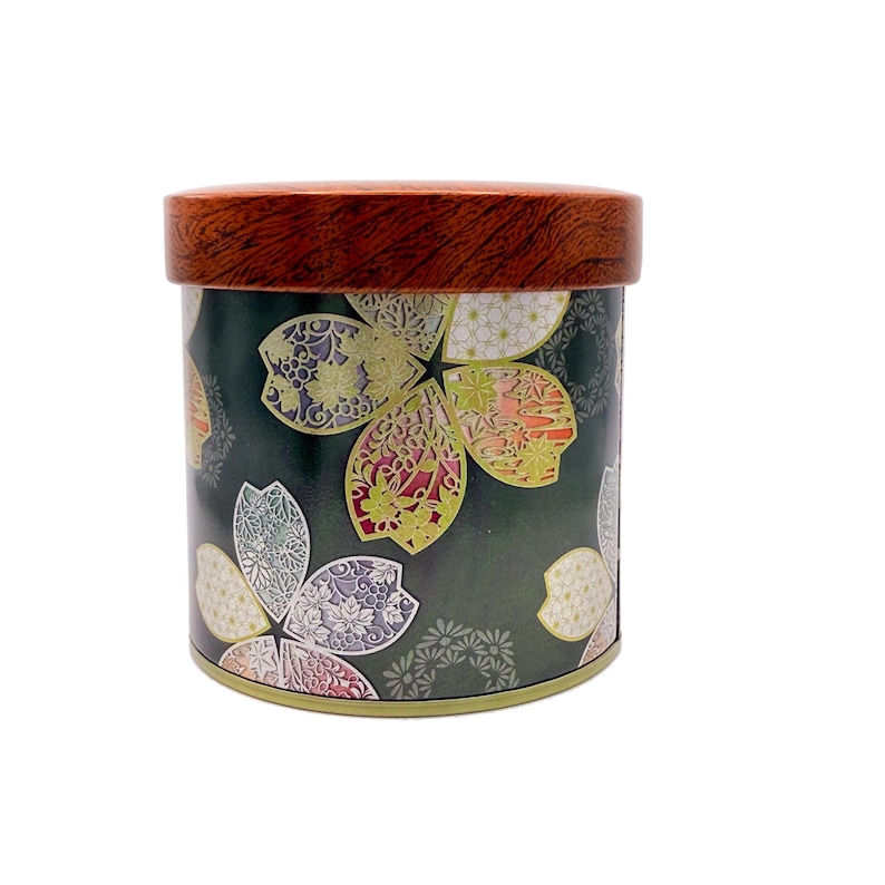 May include: A cylindrical metal storage canister featuring a dark green background decorated with a repeating pattern of stylised cherry blossom petals in shades of pink, white, and yellow. The container has a round, wood-grain patterned lid.