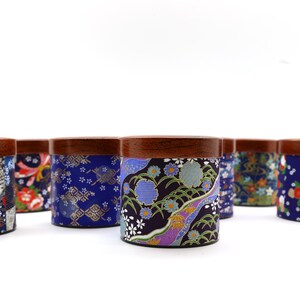 May include: A collection of cylindrical containers with dark brown wooden lids, each wrapped in fabric featuring diverse blue, purple, and red floral and geometric patterns. The containers are arranged in a group against a white background.
