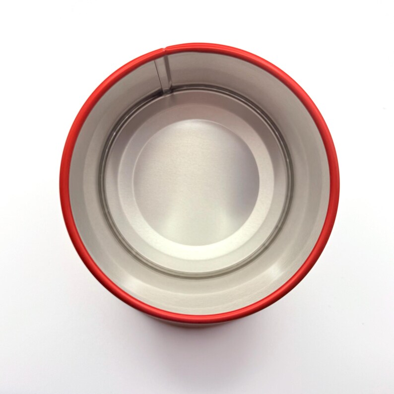 May include: A top-down view of an empty cylindrical metal tin with a bright red exterior rim and a smooth, unpainted silver-toned interior. The container features a circular base and vertical walls, showcasing a clean, industrial design.