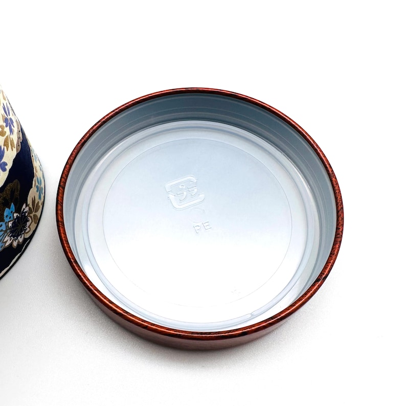 May include: A round, dark reddish-brown container lid with a smooth, glossy finish. The interior features a translucent, circular plastic insert with the embossed Japanese characters for plastic and the letters PE centred on the surface.