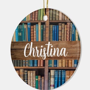 May include: Round ceramic ornament featuring a bookshelf design with various colored books. A wooden sign with the name "Christina" in white script is centered on the ornament. A gold string is attached for hanging.