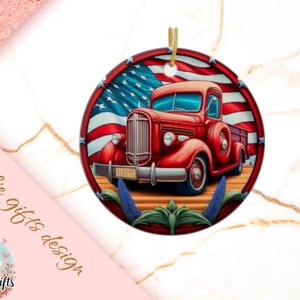 May include: A round ornament featuring a red vintage truck with an American flag background. The truck has a detailed design with blue windows and a license plate. The ornament is trimmed with a gold string for hanging.