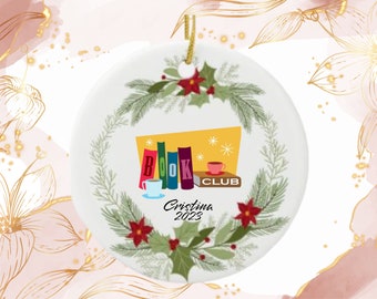 May include: White ceramic ornament with a gold string for hanging. The ornament features a "Book Club" design with colorful books, coffee cups, and the name "Cristina 2023" surrounded by a festive wreath of greenery and red poinsettias.