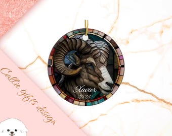 Könnte beinhalten: Runder Weihnachtsbaumschmuck mit einem Buntglasdesign, das einen Widderkopf mit filigranen Details zeigt. Der Schmuck ist mit bunten Glasstücken verziert und trägt den Namen "Xavier" und das Jahr "2024".