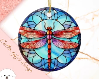 May include: A round, blue, red, and purple stained glass ornament featuring a dragonfly with intricate details. The dragonfly is centered in the ornament and has a blue background with a stained glass pattern.