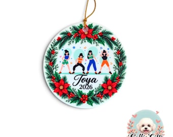 May include: A round ceramic ornament featuring a festive wreath of green pine needles, red poinsettias, and berries. The center displays four dancing figures, the name Toya, and the year 2026. A gold string is attached to the top for hanging.