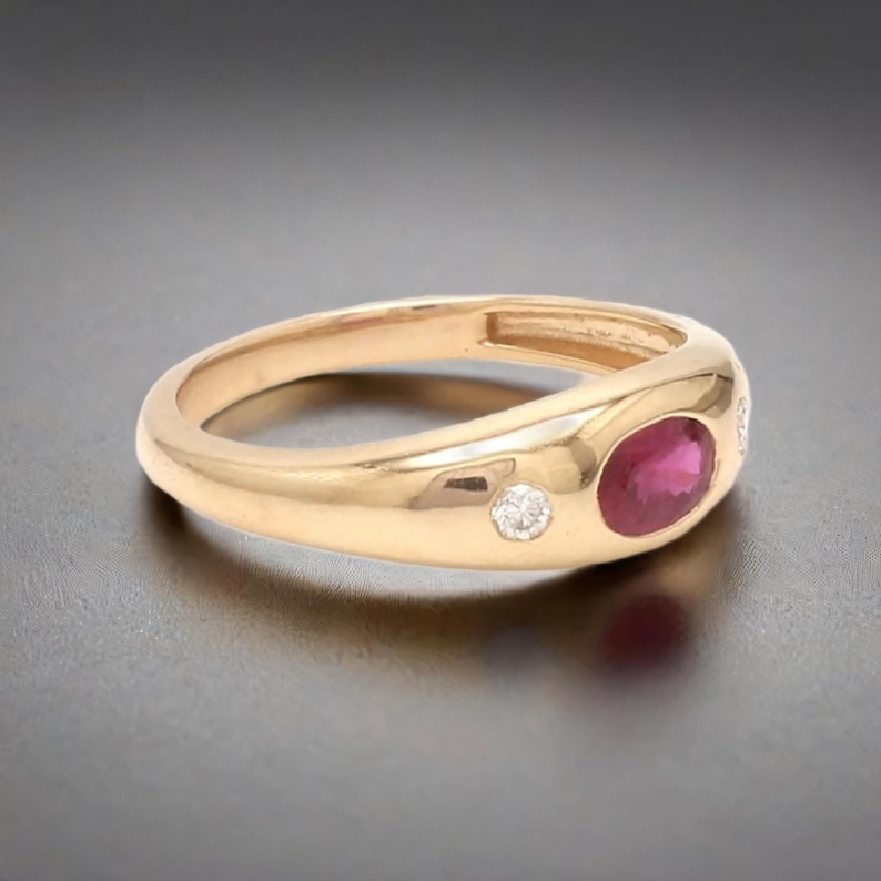 May include: A gold ring with a red ruby and two small diamonds. The ring is set in a smooth, rounded band.