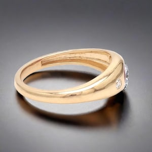 May include: A gold band ring with a single round diamond set in the center and two smaller diamonds on either side.