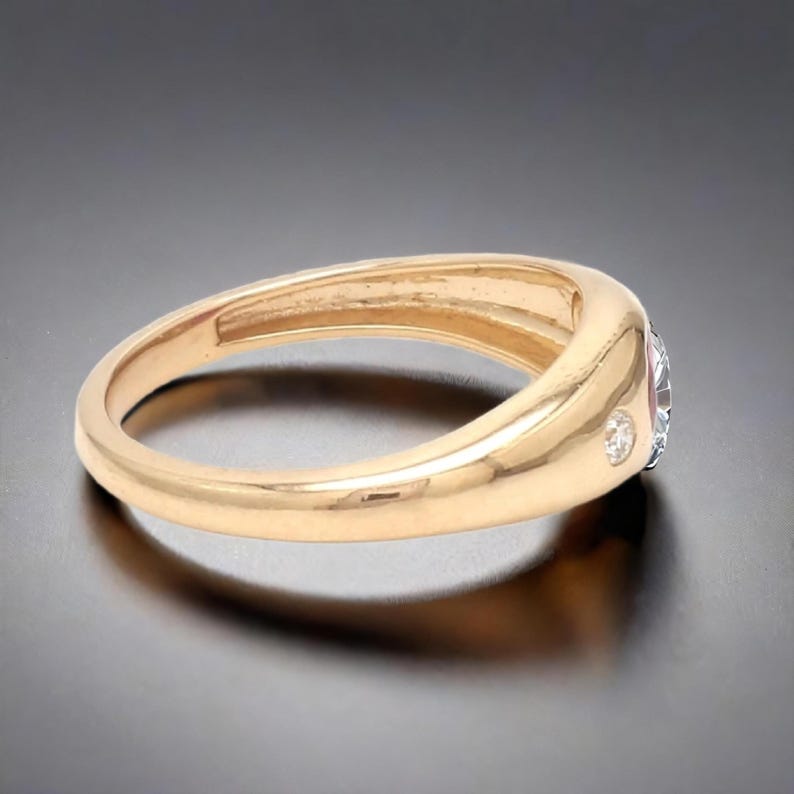May include: A gold band ring with a single round diamond set in the center and two smaller diamonds on either side.