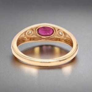 May include: A gold ring with a red oval gemstone and two smaller white gemstones on either side.