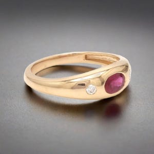 May include: A gold ring with a red ruby and two small diamonds. The ring is set in a smooth, rounded band.