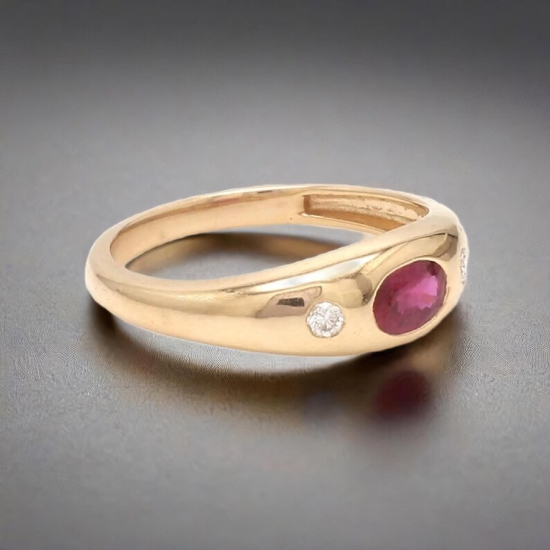 May include: A gold ring with a red ruby and two small diamonds. The ring is set in a smooth, rounded band.