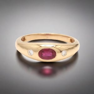 May include: A gold ring with a red ruby and two small diamonds. The ring is set in a smooth, rounded band.