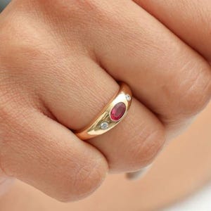 May include: A gold ring with a red oval gemstone and two smaller clear gemstones.