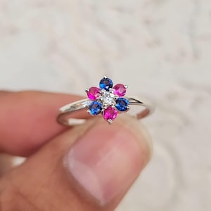 May include: A silver ring with a flower design featuring pink, blue, and white gemstones.