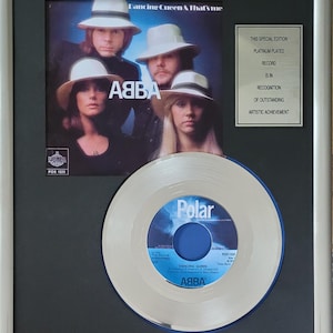 Op de afbeelding: Ingelijste platina-geplateerde plaat van ABBA's "Dancing Queen". De lijst bevat de albumhoesafbeelding en een plaquette met de erkenning van de uitstekende artistieke prestatie van de plaat. De plaat zelf is zilverkleurig met een blauw midden.
