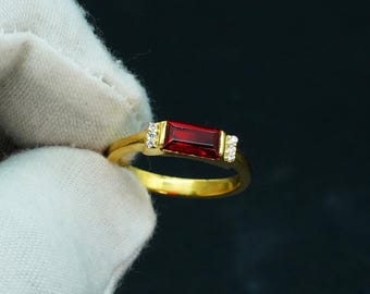 May include: A gold ring with a red rectangular gemstone and small clear stones on the band.