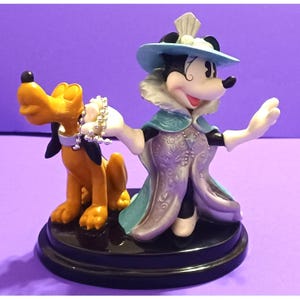 May include: A Minnie Mouse figurine in a light blue hat and cape, holding a pearl necklace that is around Pluto's neck. The figurine is on a black base, with a purple background.