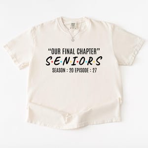 May include: A cream-colored short-sleeve t-shirt featuring black text that reads "OUR FINAL CHAPTER" at the top, "SENIORS" in the center with colorful dots between letters, and "SEASON : 20 EPISODE : 27" printed in black at the bottom.