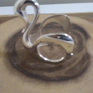 May include: A silver swan-shaped napkin holder. The holder is made of metal and has a smooth, polished finish.