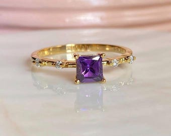 May include: A gold ring with a square purple amethyst gemstone and small clear gemstones set in the band.
