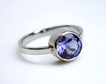May include: A silver ring featuring a large, round, faceted, light purple gemstone. The gemstone is set in a bezel setting, and the band is smooth and polished. The ring is displayed on a white background.