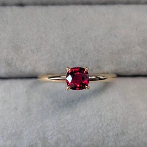 May include: A gold ring with a red gemstone set in a square shape.