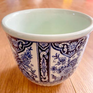 May include: A white ceramic planter with a blue and black floral design. The planter has a scalloped rim and a smooth, glazed finish.