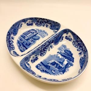 May include: Oval divided serving dish with a blue and white landscape design. The dish is divided into two sections and features a detailed floral border. The blue and white color scheme gives it a classic, vintage look.