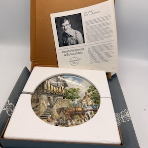 May include: A decorative plate by Josiah Wedgwood & Sons Limited, featuring a detailed painting of a rural scene with horses and a building. The plate is in its original box with protective foam and a biography of the artist, John L. Chapman.