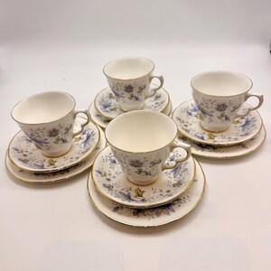 以下が含まれることがあります： 青と金のトリムのフローラルパターンが施された、白のティーカップとソーサーの5客セット。 ティーカップは繊細なデザインで、ソーサーは丸いです。 セットは白い表面に配置されています。