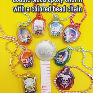May include: A collection of double-sided epoxy charms, each featuring a unique cartoon character design. The charms are approximately 1 inch (25.4mm) in size and come with a colored bead chain. Text on the image reads "they're so smol!!!".