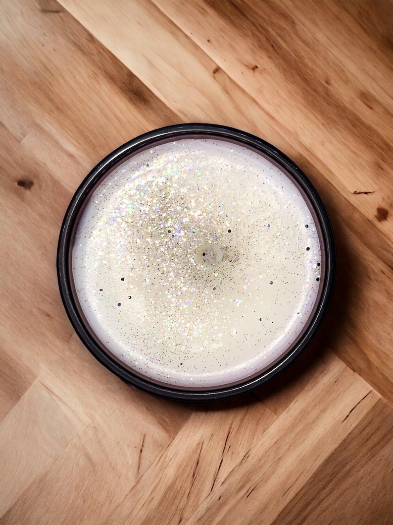 May include: A white candle with silver glitter in a black jar.