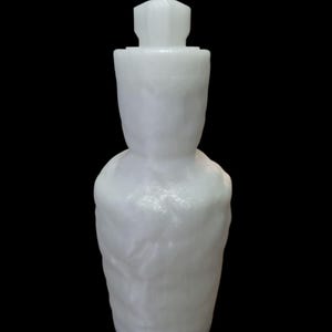 May include: A white, textured bottle with a geometric stopper. The bottle has a rounded base and a cylindrical body that tapers towards the neck. The stopper is a small, multi-faceted shape. The background is solid black.