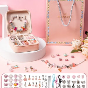 Könnte beinhalten: Rosa Schmuckbox mit einem Charm-Armband und einer Vielzahl von Charms, Perlen und Abstandshaltern. Die Box ist geöffnet und die Charms werden in den Fächern ausgestellt. Die Box ist in einer rosa Geschenktüte verpackt, auf der "Princess You are my little princess, beautiful" steht.