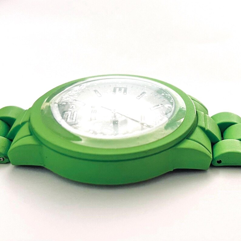 May include: A bright green wristwatch with a clear face. The watch has a matching green band and a white watch face with black numerals. The watch is set against a white background.