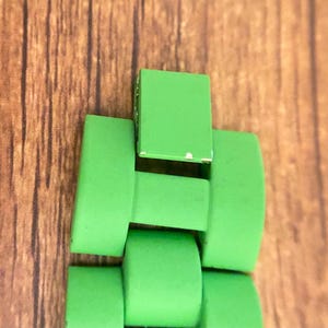 May include: Close-up of a bright green watch band, featuring rectangular and curved links. The band is made of a solid, vibrant green material, with a few minor imperfections. The background is a wooden surface.
