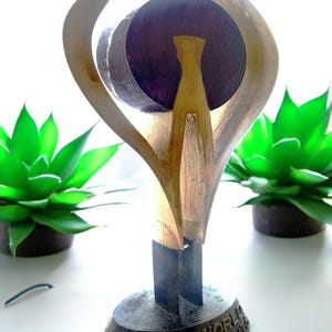 May include: A gold-colored, abstract sculpture with a circular base. The base is inscribed with the words "Oddworld Inhabitants".
