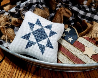 May include: A white fabric pillow with a blue star design, sitting on a metal tray with a wooden surface. The tray is decorated with a wooden heart-shaped American flag with white stars and red and blue stripes.