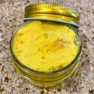 May include: A glass jar filled with a bright yellow, creamy substance, with a gold lid on top.
