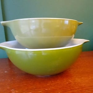 May include: Two green mixing bowls, one nested inside the other. The top bowl is a lighter shade of green and the bottom bowl is a darker shade of green.