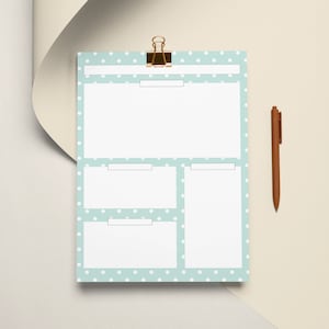 May include: A light blue and white polka dot notepad with a gold binder clip and a brown pen. The notepad has four sections for notes and lists. The pen is positioned to the right of the notepad on a cream-colored surface.