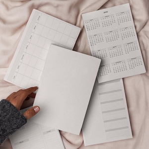 Puede incluir: Un conjunto de tres cuadernos en blanco con páginas cuadriculadas, rayadas y de calendario. Las páginas del calendario son para el año 2023.