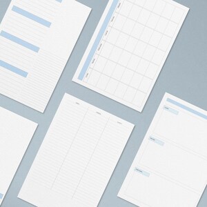 May include: A collection of white planner pages with light blue accents. The pages feature various layouts, including lined sections, a monthly calendar grid, and daily planning templates. The pages are arranged on a light gray background.