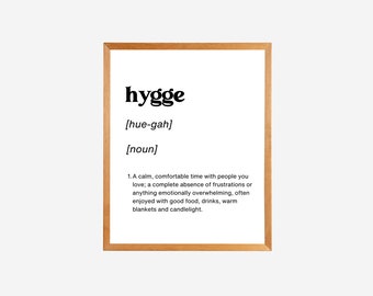 Könnte beinhalten: Ein gerahmter Druck mit einer Definition des Wortes "hygge" in einer einfachen, modernen Schriftart. Die Definition beschreibt Hygge als eine ruhige, gemütliche Zeit mit geliebten Menschen, frei von Frustrationen, oft genossen mit gutem Essen, Getränken, warmen Decken und Kerzenlicht.