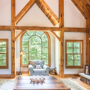 May include: A large living room with exposed wooden beams and a stone fireplace. The room has a large arched window, two smaller windows, and a couch with a throw pillow.