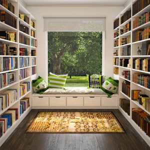 May include: A white built-in bookcase with a window seat and a patterned rug. The window seat has white cushions and pillows with green and black patterns. The bookcase is filled with books.