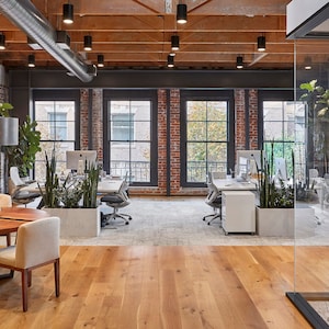 Könnte beinhalten: Ein moderner Büroraum mit Sichtbacksteinwänden, großen Fenstern und einem Holztisch mit Stühlen. Der Raum ist mit Pflanzen dekoriert und hat eine Glaswand.