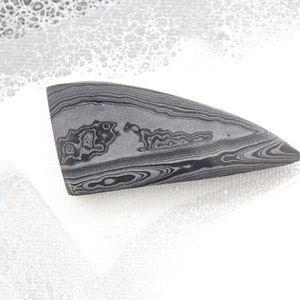 May include: A gray and black banded agate cabochon with a pointed shape. The agate has a swirling pattern of dark gray and black bands.