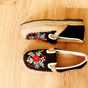 Op de afbeelding: Twee paar zwarte canvas schoenen met geborduurde bloemenmotieven. De schoenen hebben een jute zool en een witte rand rond de bovenkant.